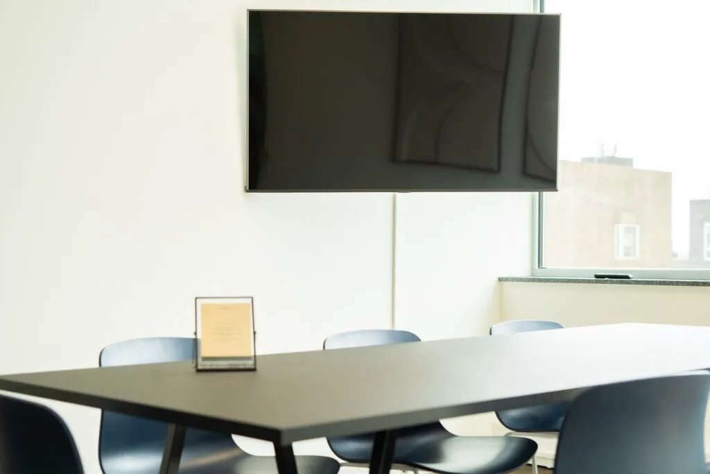 Vergaderruimte aan de Joop Geesinkweg met een zwarte tafel, blauwe stoelen en een flatscreen aan de muur.